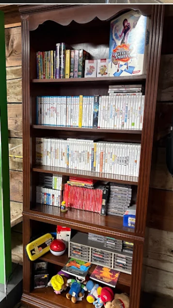 Floor-to-ceiling shelf of Wii, DS, and 3DS games with handhelds and toys